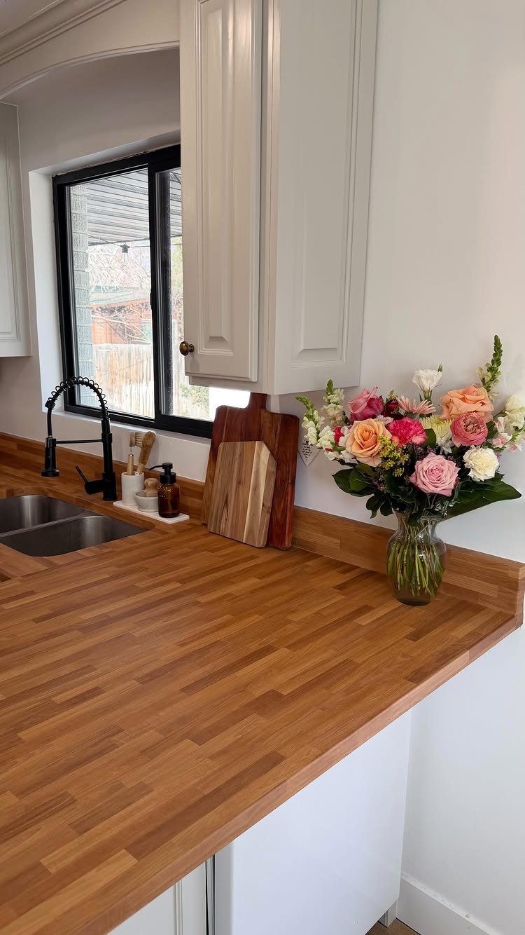 Butcher block countertop in a small kitchen with white cabinets and fresh roses.