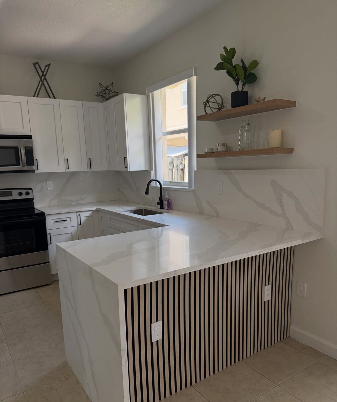 White marble-patterned kitchen countertops and backsplash with wooden floating shelves and white cabinets.