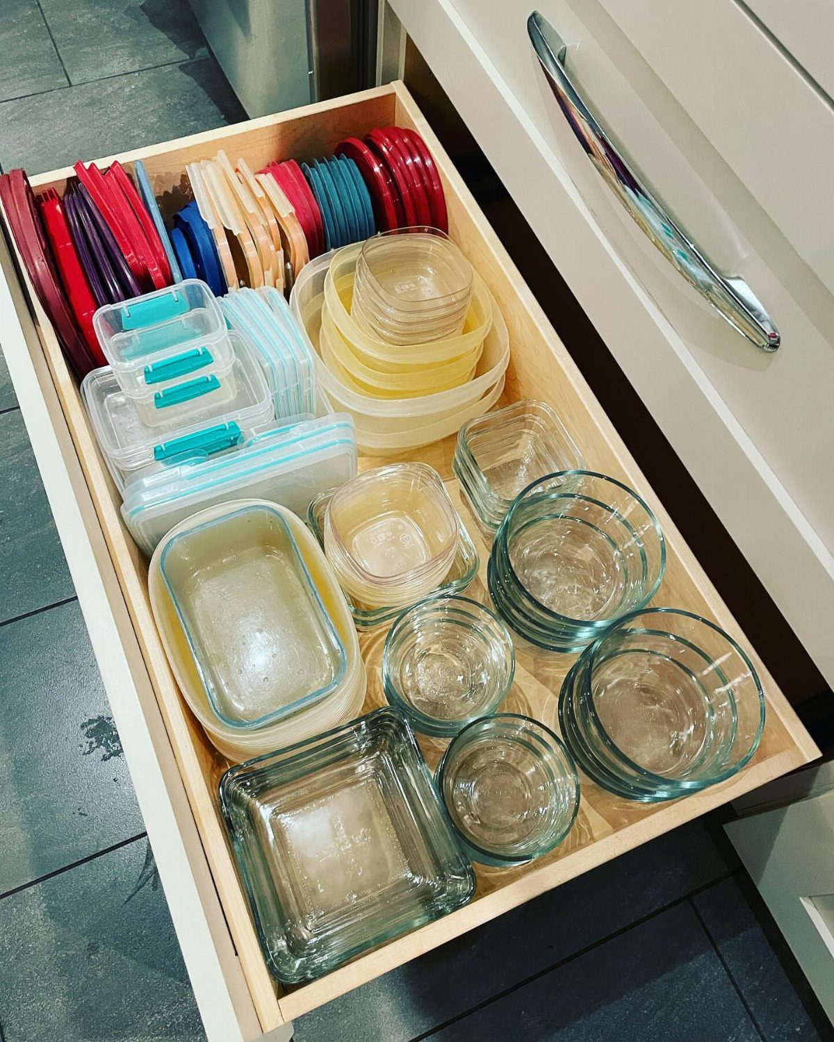 Open kitchen drawer with organized glass and plastic food storage containers and lids.