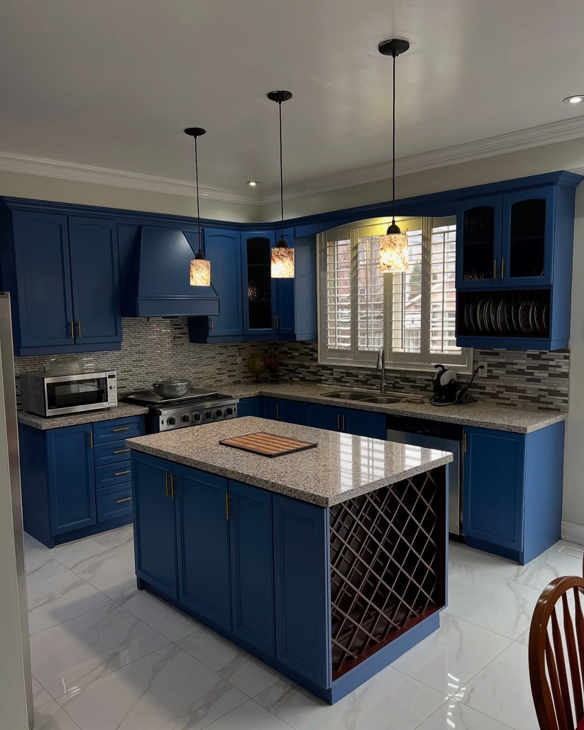 Deep blue kitchen cabinets with a granite island and hanging pendant lights.