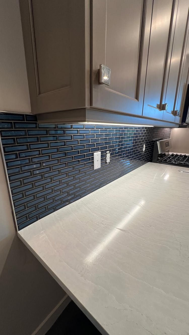 White marble kitchen countertop with dark blue brick backsplash and grey cabinets.