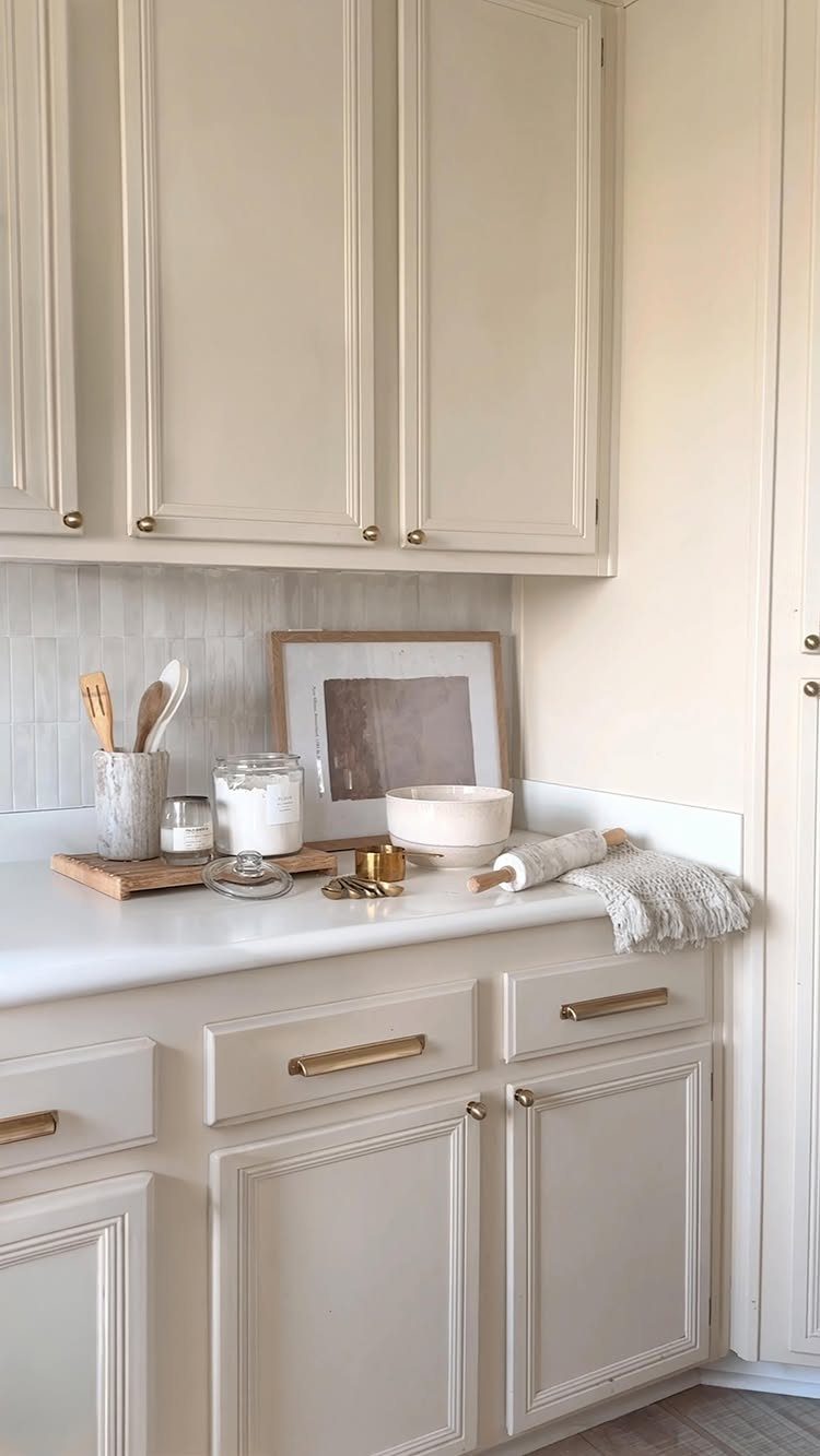 Cream kitchen cabinets with gold handles and a white countertop with decor.