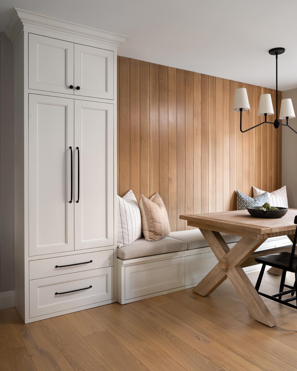 Wooden dining table with a white built-in bench seat against a wood paneled wall.
