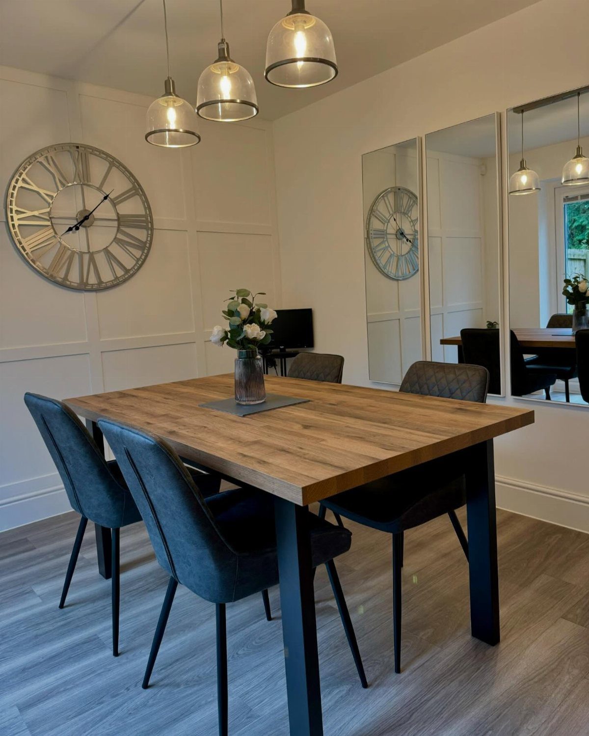 Wooden dining table with grey chairs and tall vertical mirrors on the wall