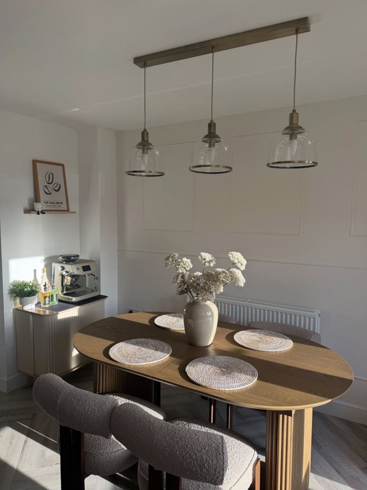 Oval wooden dining table with woven placemats and grey chairs in white room.
