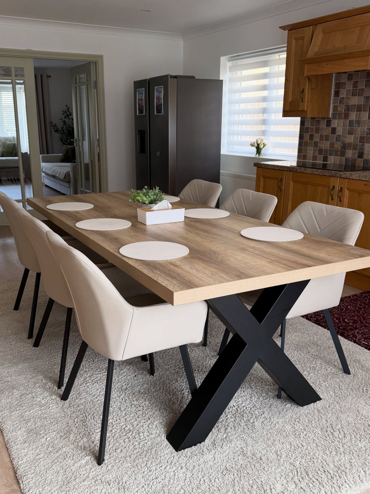 Wooden dining table with beige chairs on a light grey shag rug in kitchen