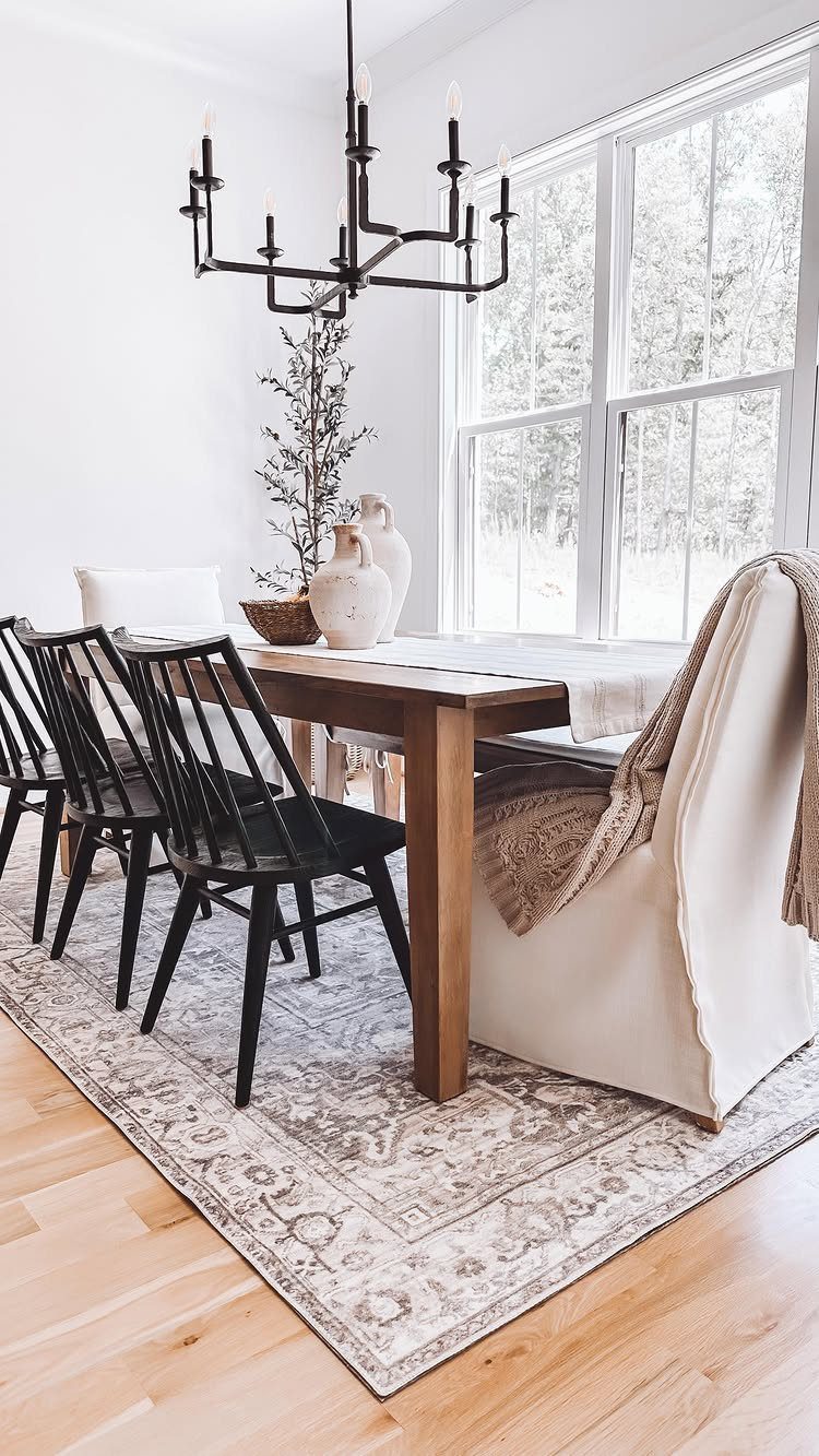 Wooden dining table and black chairs on a patterned grey area rug.