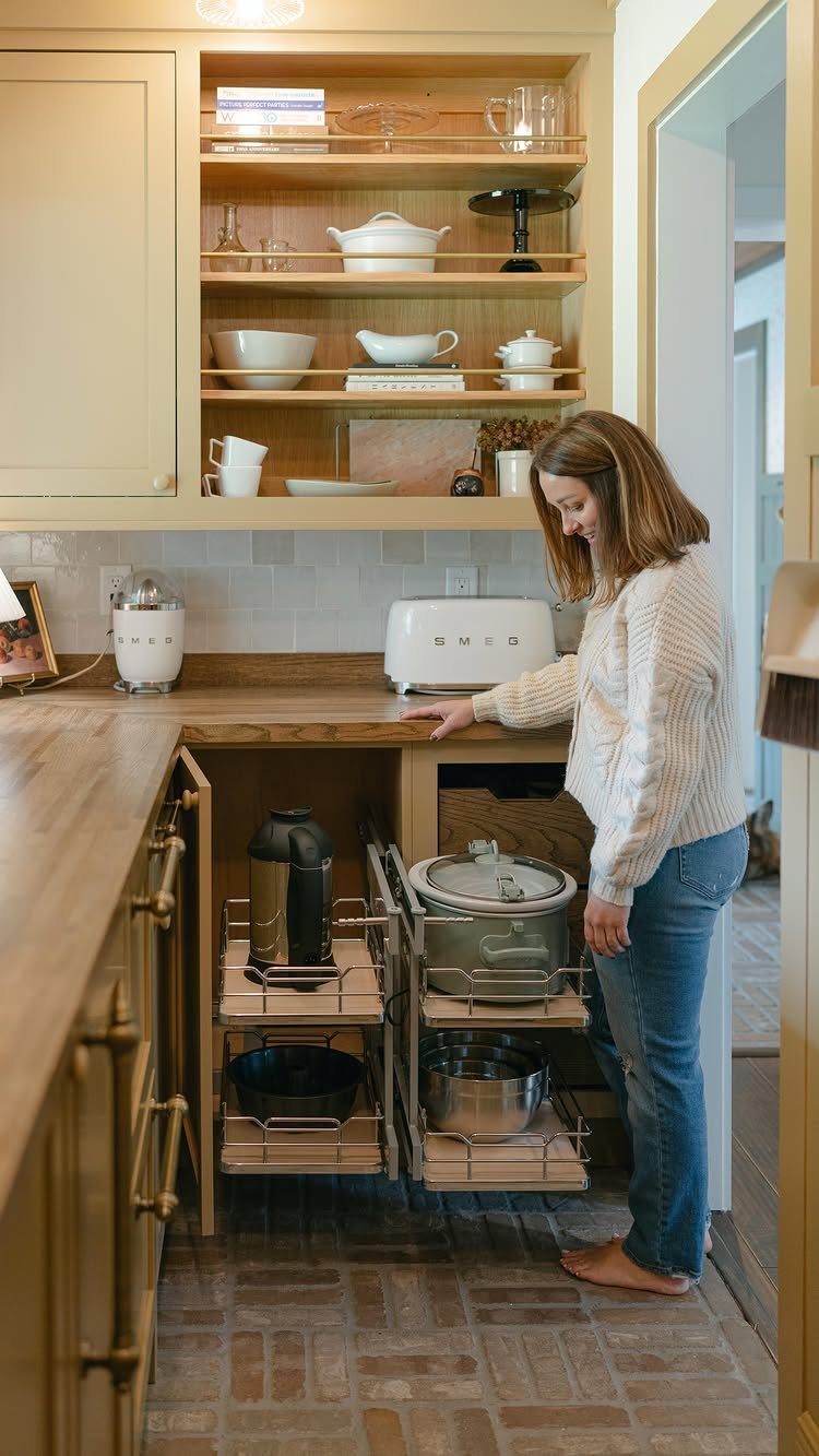 Woman pulling out a multi-tiered metal storage rack from a blind corner kitchen cabinet.