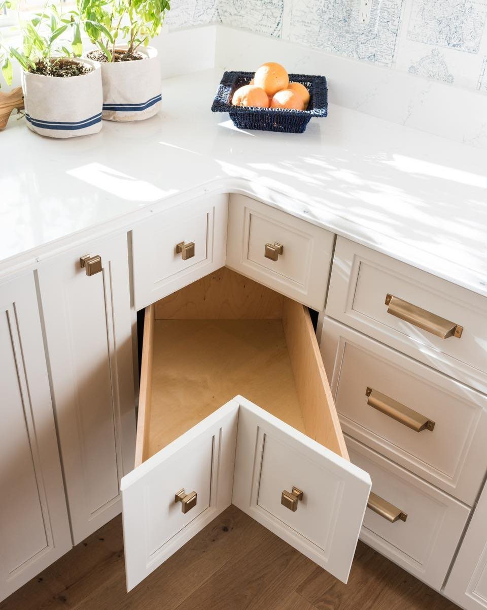 Open V-shaped corner drawer in a white kitchen with gold hardware and white countertops.