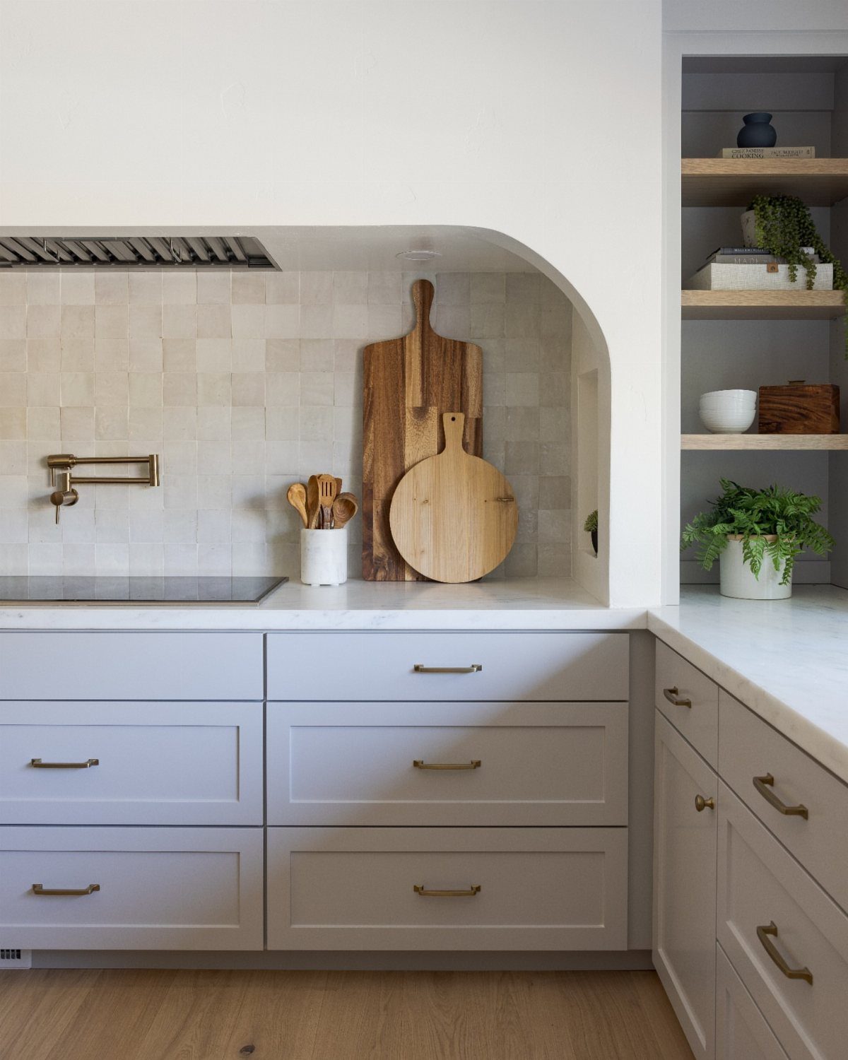 Open wooden corner shelves in a white kitchen holding plants and kitchenware.