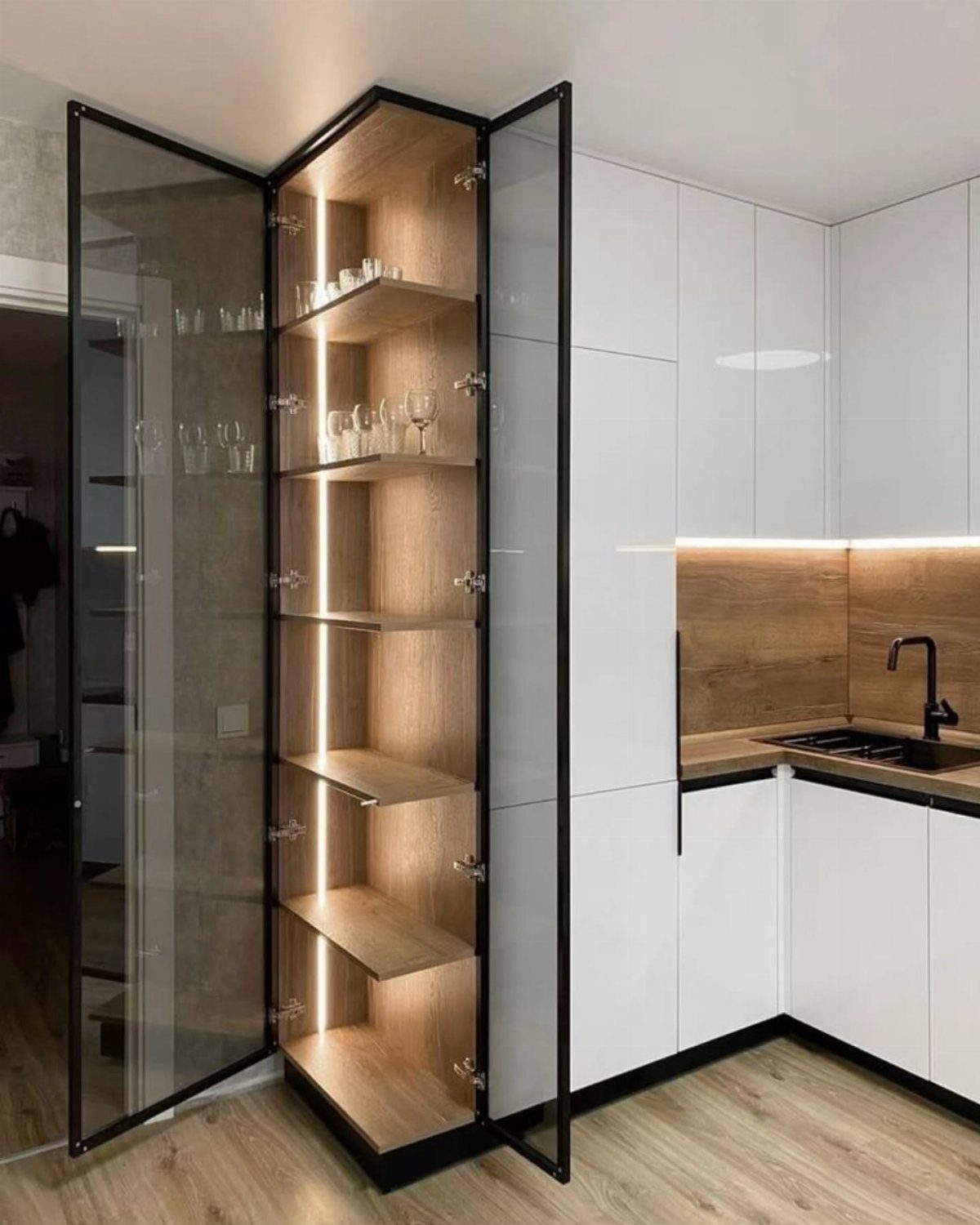 Tall corner cabinet with glass doors and integrated lighting showcasing glassware in kitchen.