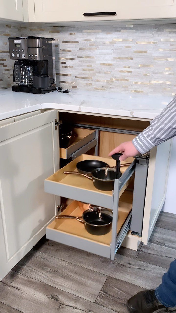 Magic corner pull-out shelving system in a white kitchen cabinet holding frying pans.