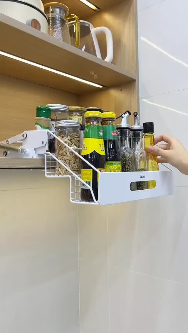 White pull-down shelf mechanism in a wooden cabinet holding various condiment bottles.