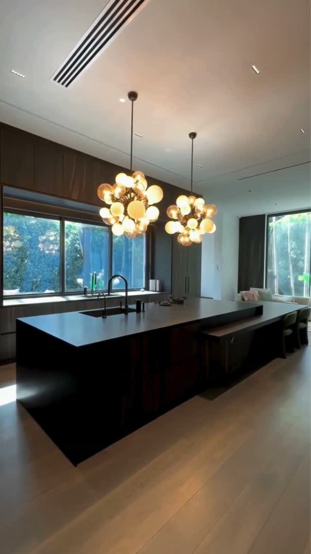 Black kitchen island with black countertops and gold spherical pendant lights.