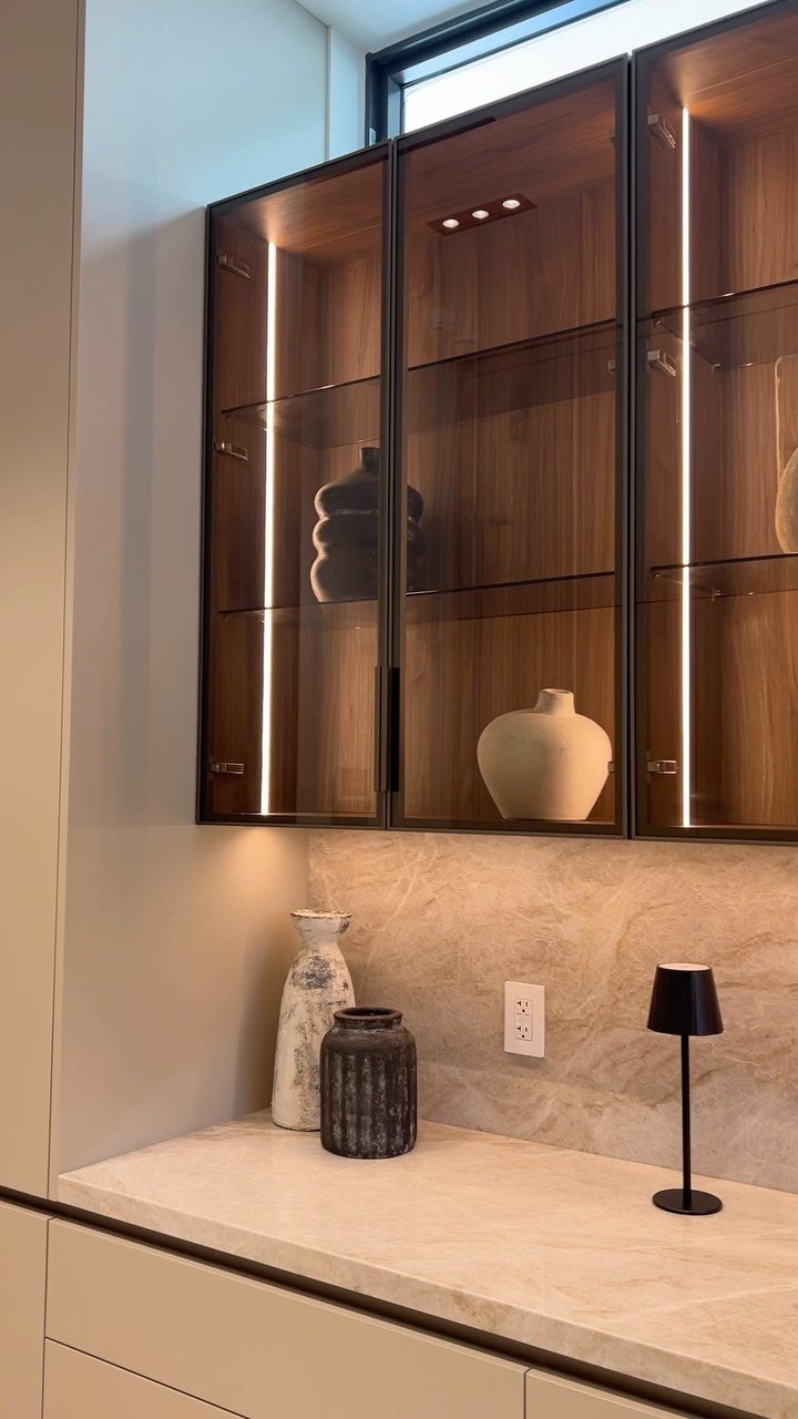Dark brown cabinets with glass-paneled doors and interior lighting over a marble countertop.