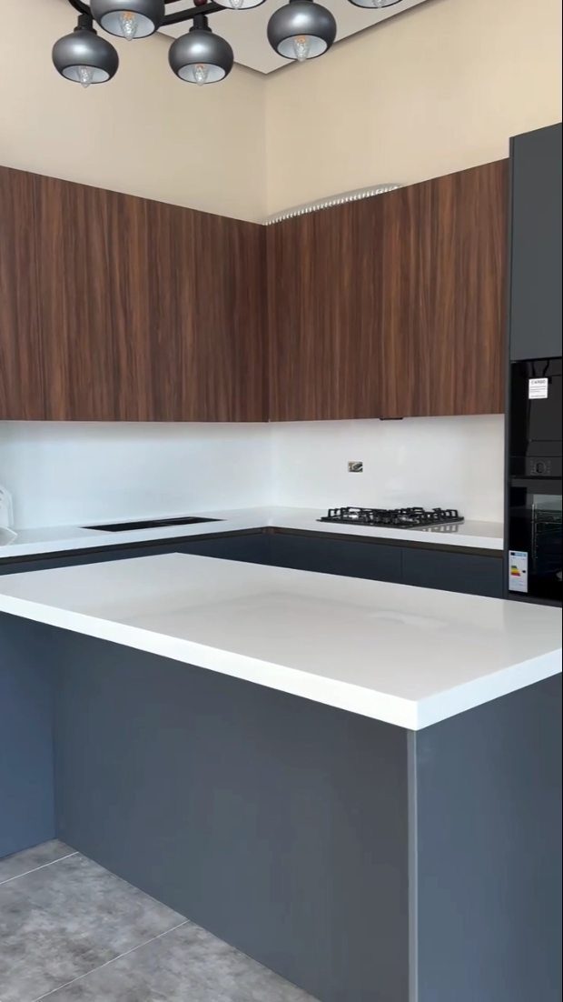 Dark grey kitchen cabinets and island with bright white countertops and wood upper cabinets.