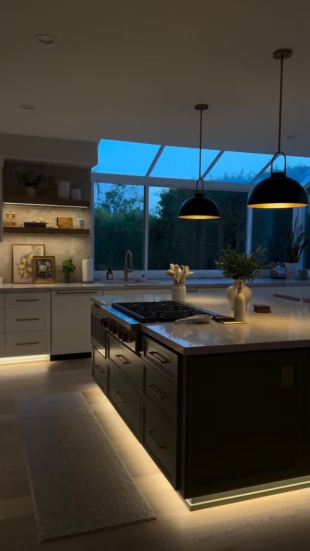 Dark kitchen island with white countertops and warm under-cabinet lighting at the base.