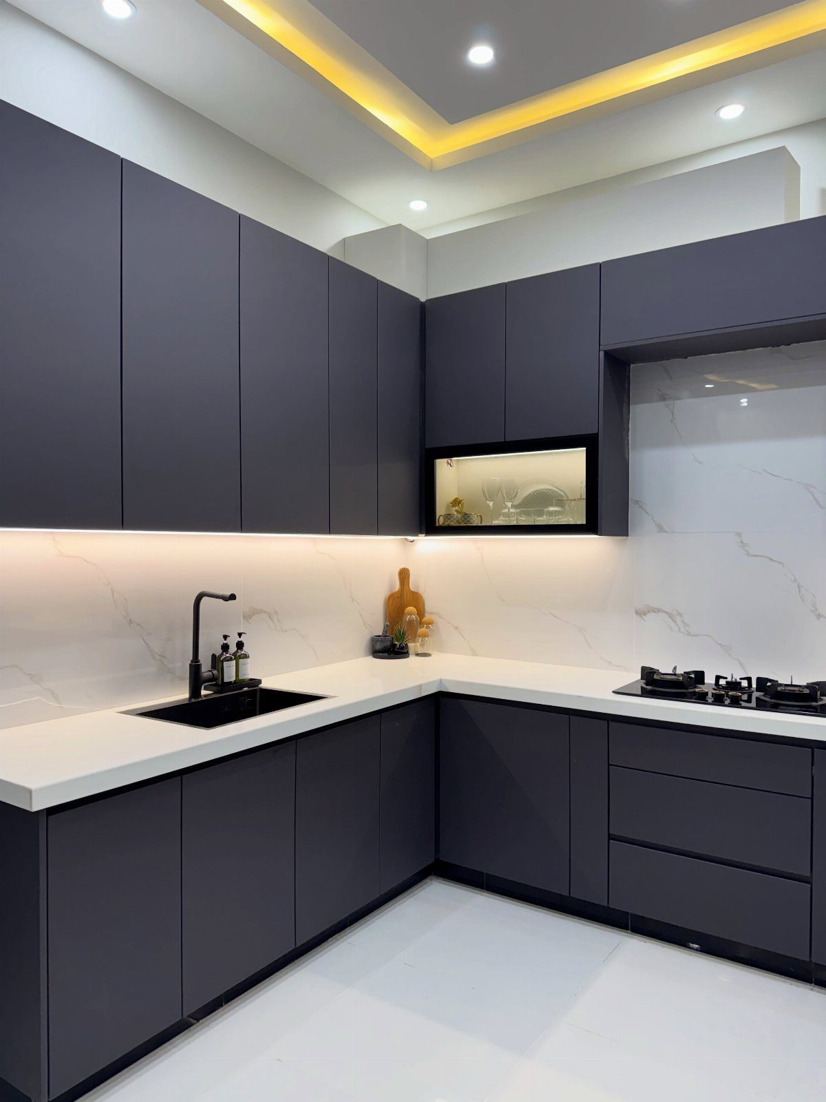 Modern kitchen with dark grey cabinets, white countertops, and recessed ceiling lighting.