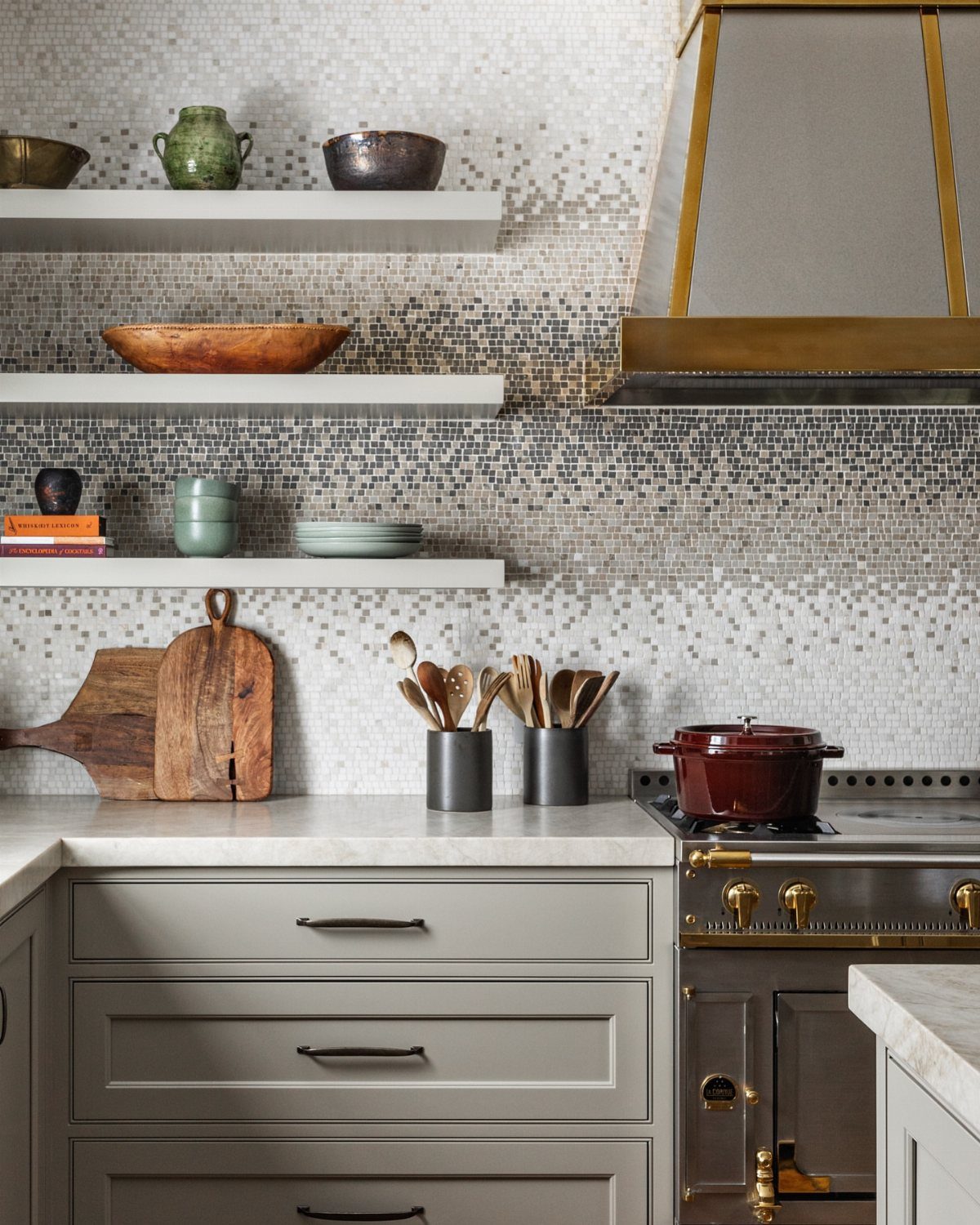 Mosaic tile backsplash with a grey gradient above grey kitchen cabinets and shelves.