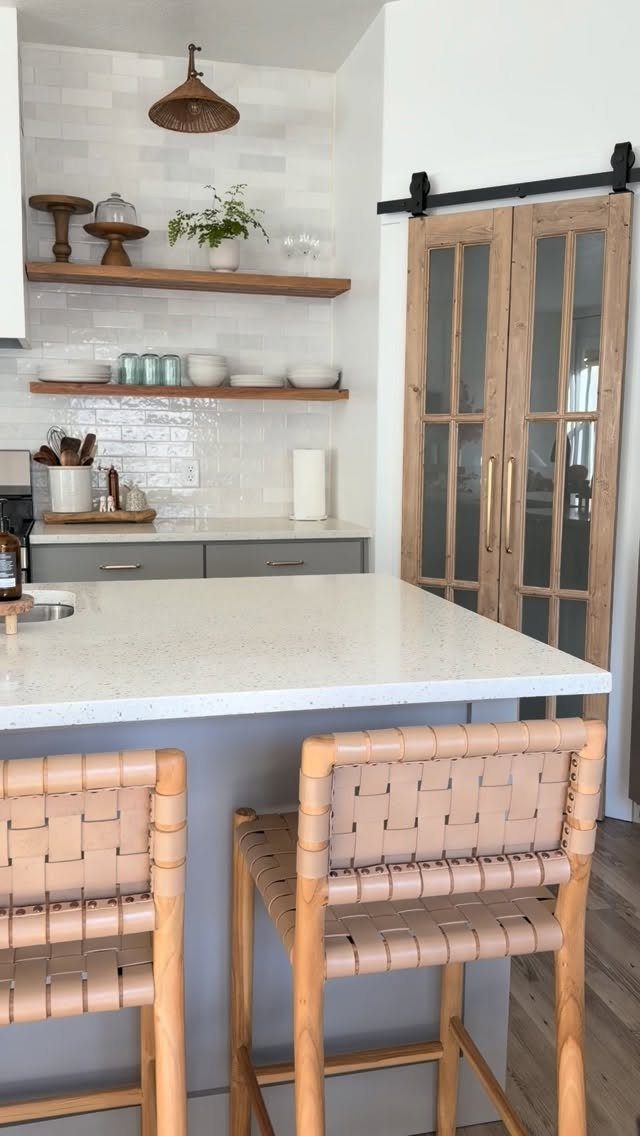 Grey kitchen island with white countertop and two woven leather bar stools.