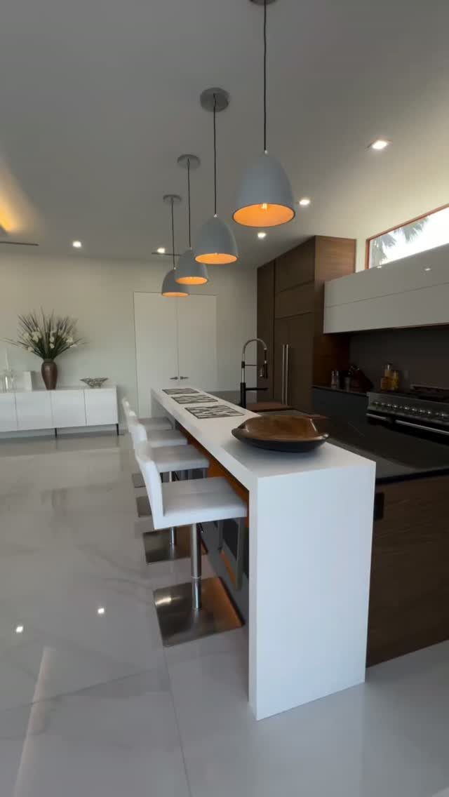 Modern kitchen with a narrow white island, white bar stools, and grey pendant lights.