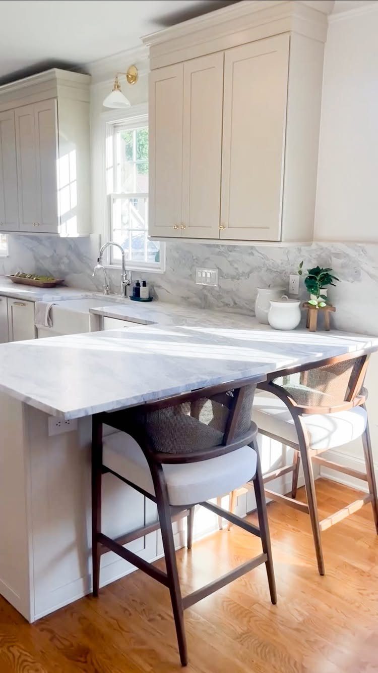 White kitchen peninsula with marble countertop and two wooden bar stools with cushions.