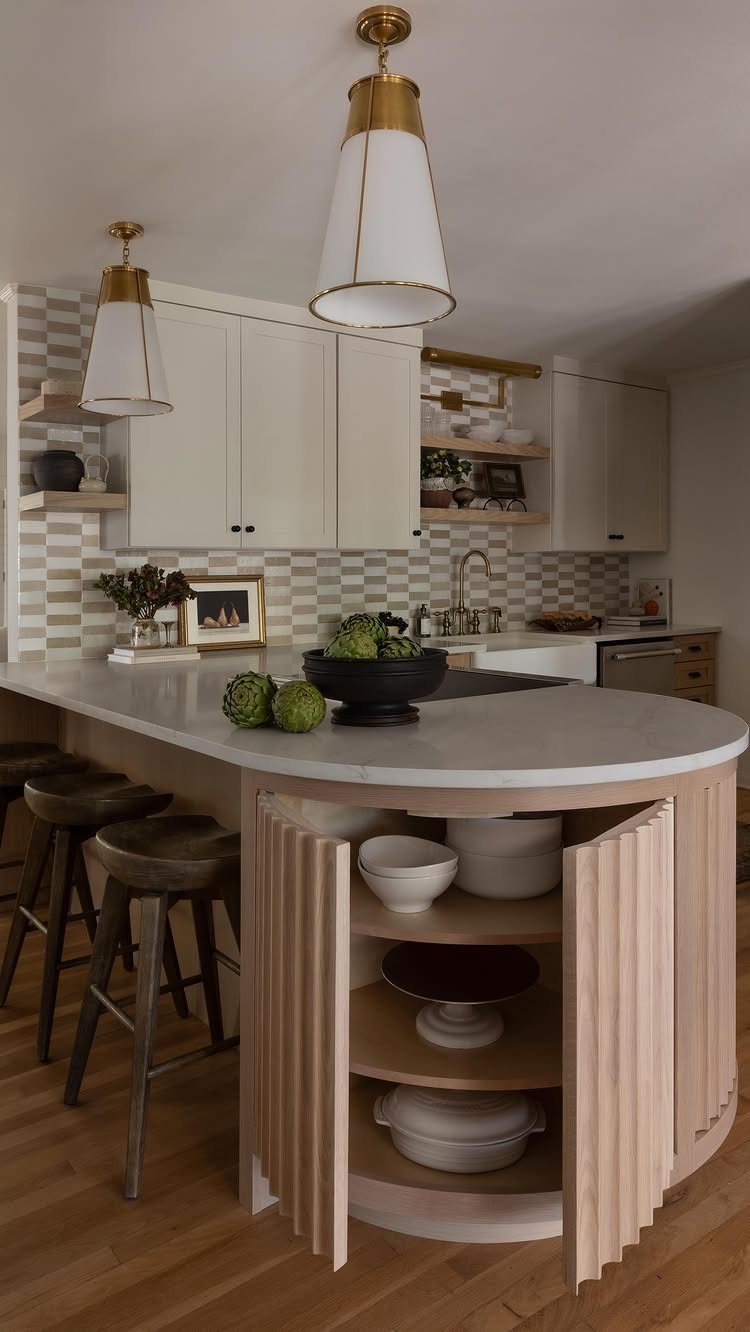 Small white marble kitchen island with wooden stools and gold pendant lighting.