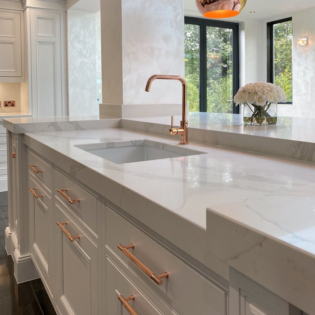 White kitchen island with marble countertop, copper faucet, and white cabinetry.