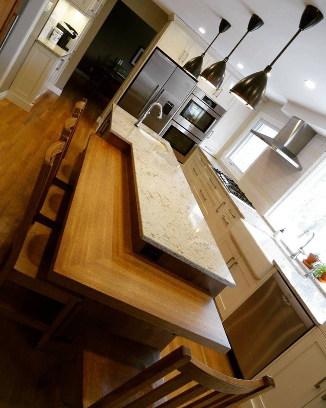 Two-tiered kitchen island with white marble countertop and lower wooden dining ledge.
