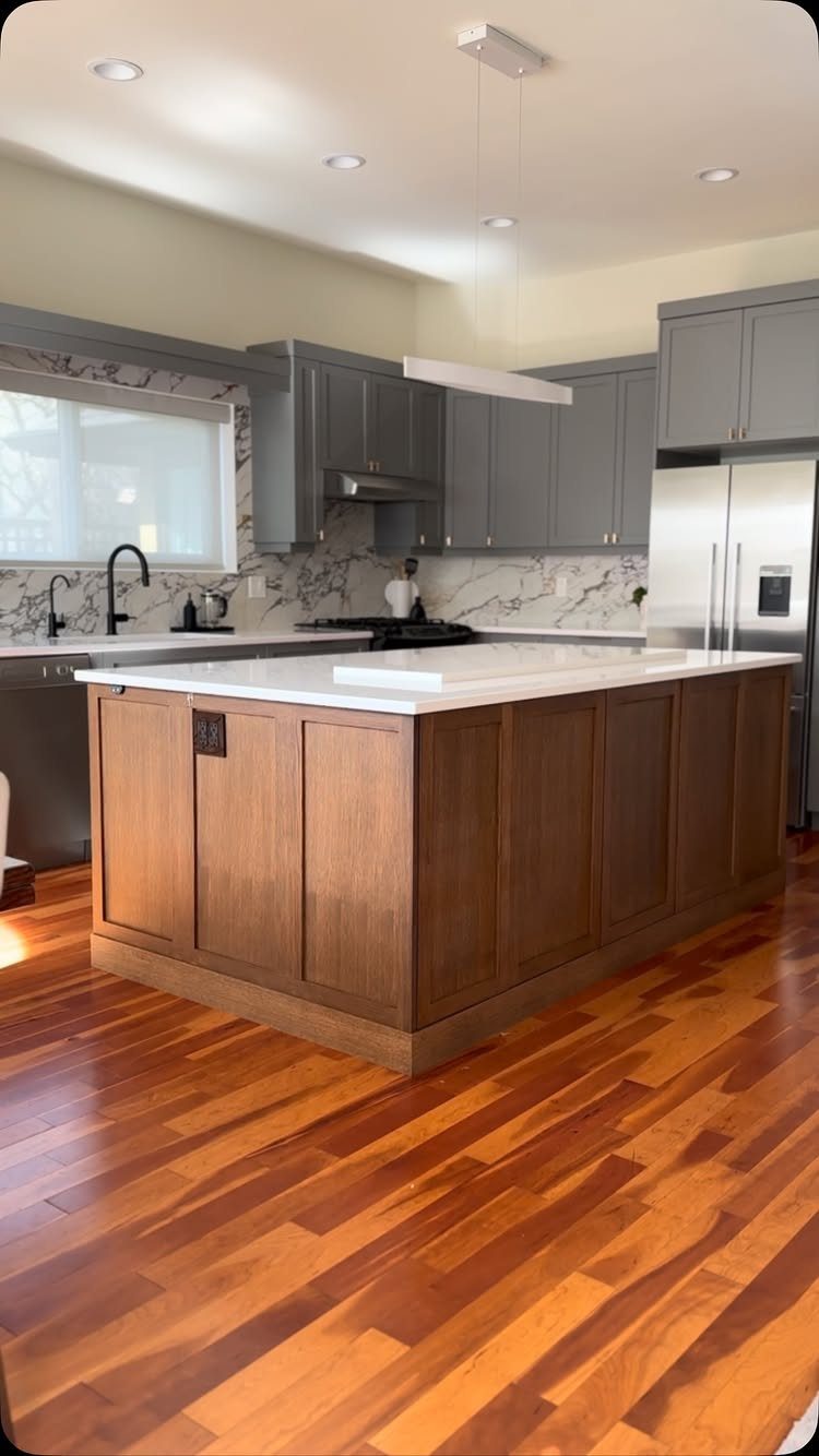 Wooden kitchen island with white countertop in a room with grey cabinets.