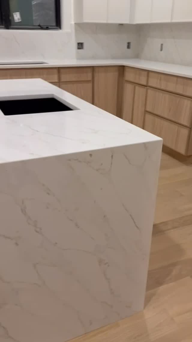 White marble-patterned quartz island and countertops with light wood kitchen cabinets.