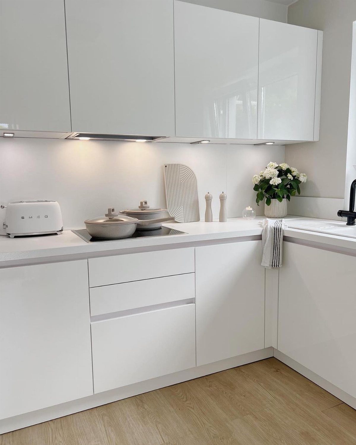 Small white kitchen with glossy cabinets, white countertops, and light wood floors.