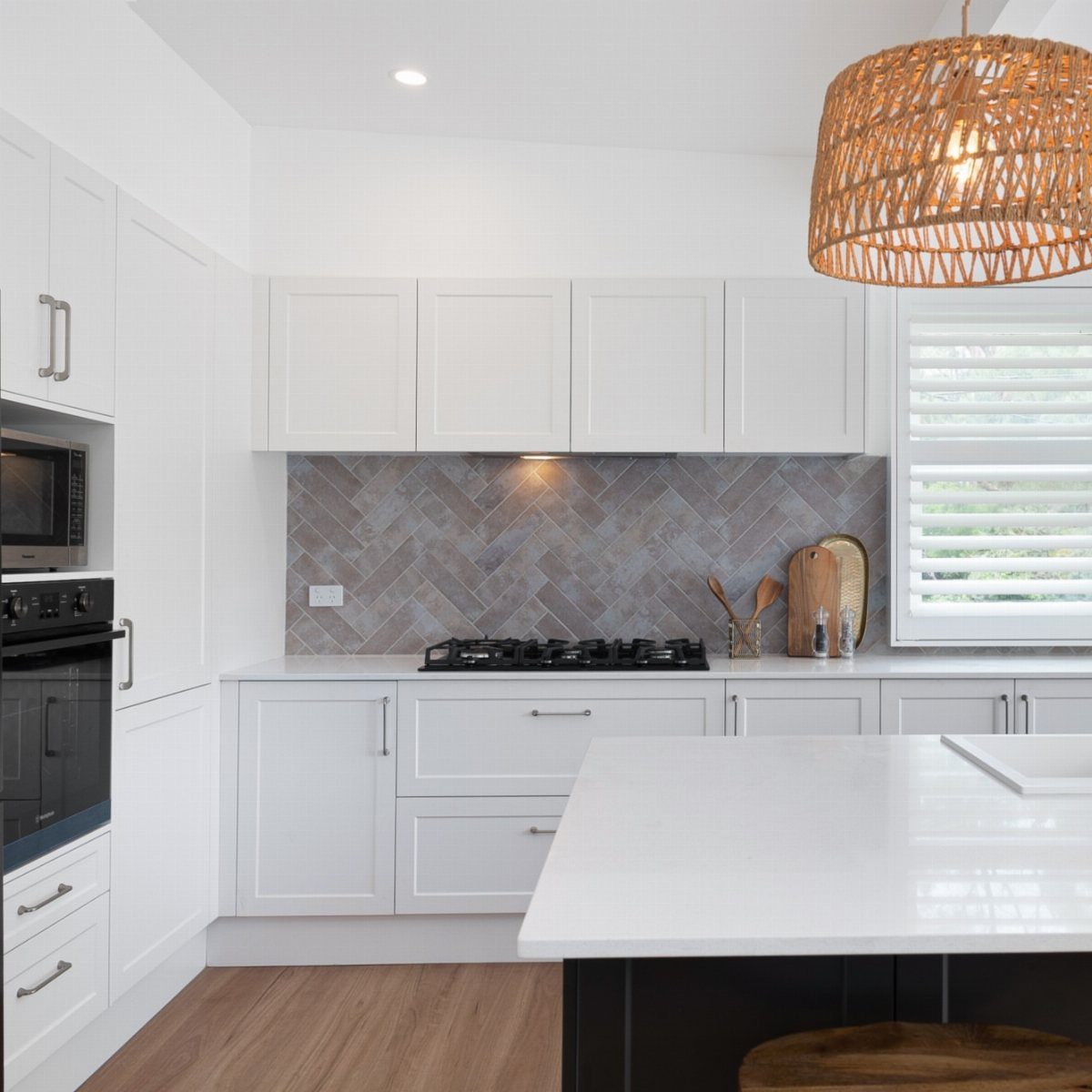 Modern kitchen with white quartz countertops, grey herringbone backsplash, and woven pendant light.