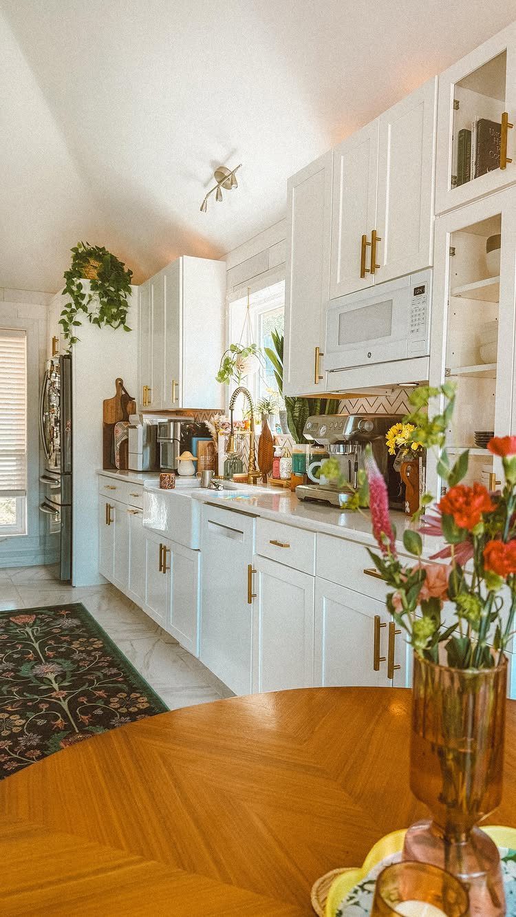 Kitchen with white cabinets and countertops featuring trailing green plants and colorful flowers.