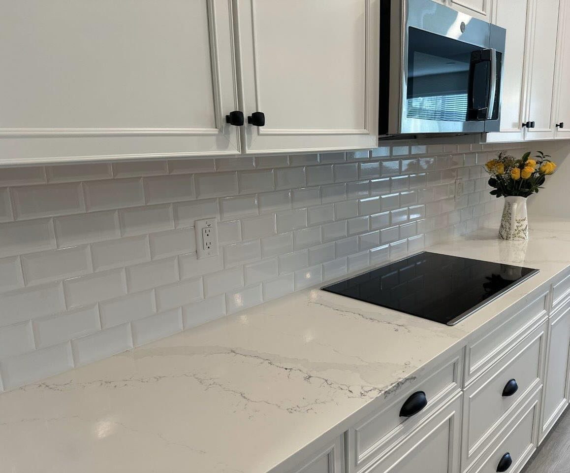 White subway tile backsplash behind a white quartz countertop in a modern kitchen.