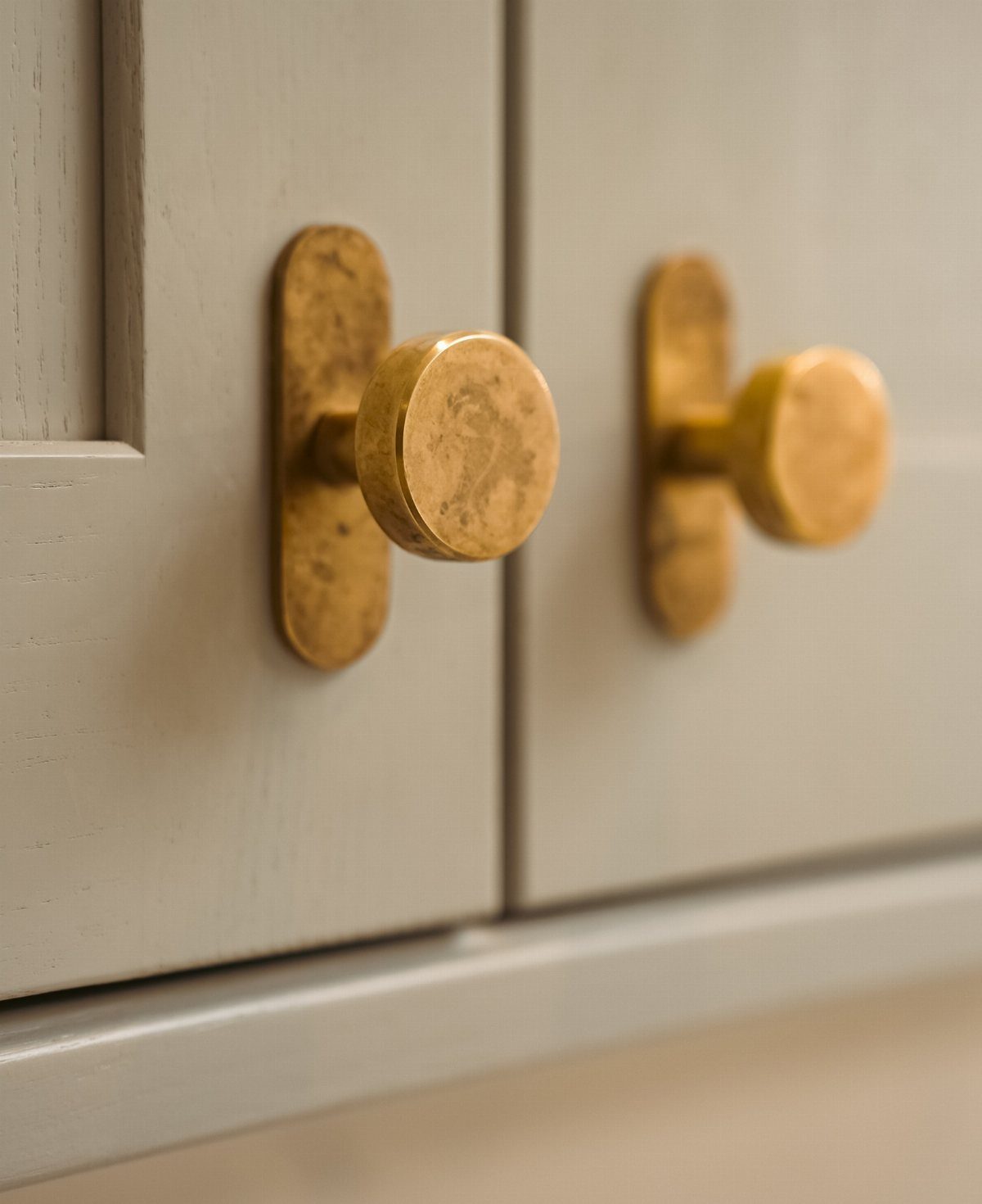 Round brass cabinet knobs with backplates on light grey wooden doors.