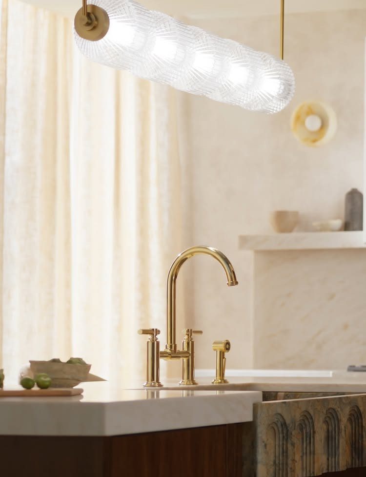 Polished brass faucet on a white marble kitchen counter with a glass pendant light.