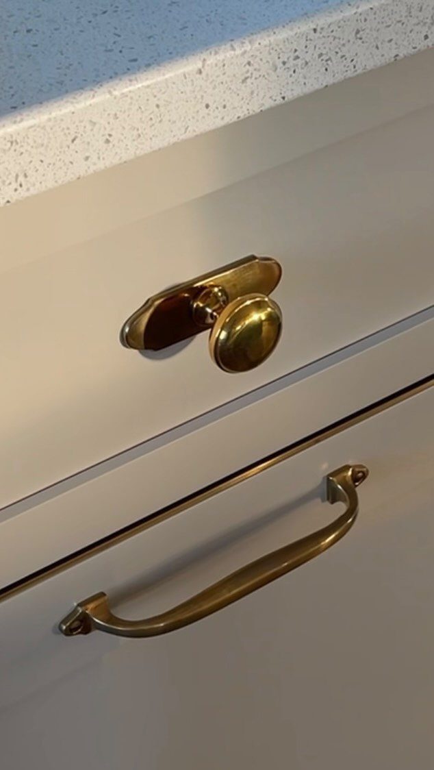 Polished brass knob and handle on white kitchen drawers with speckled countertop