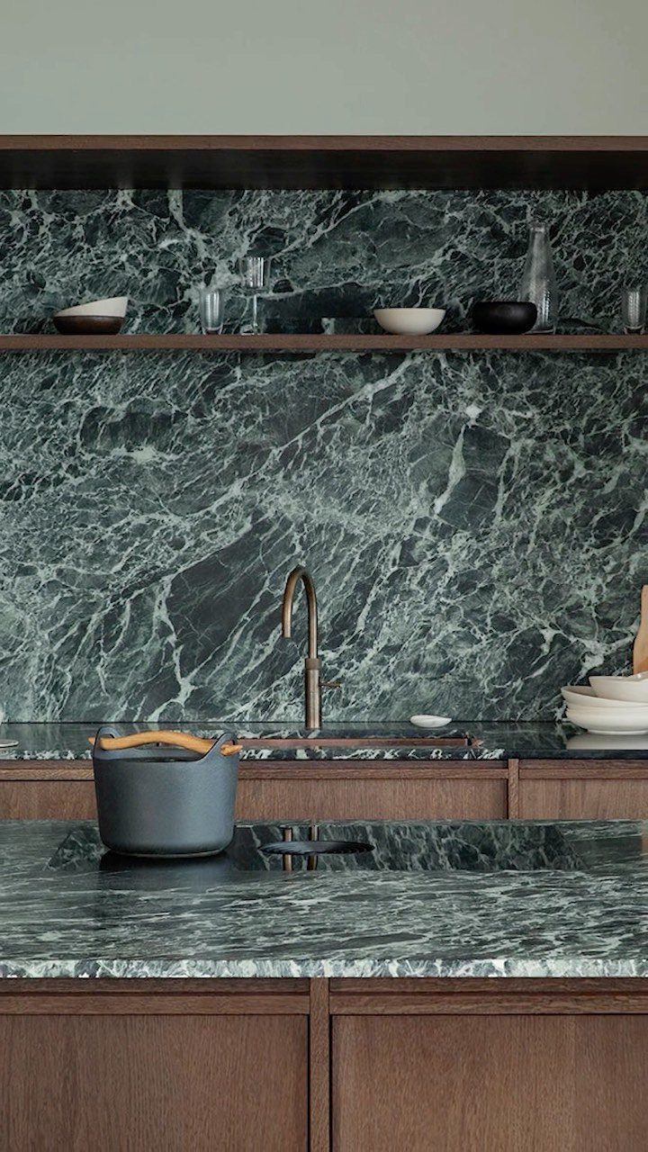 Dark stained wood kitchen cabinets with green marble countertops and backsplash.