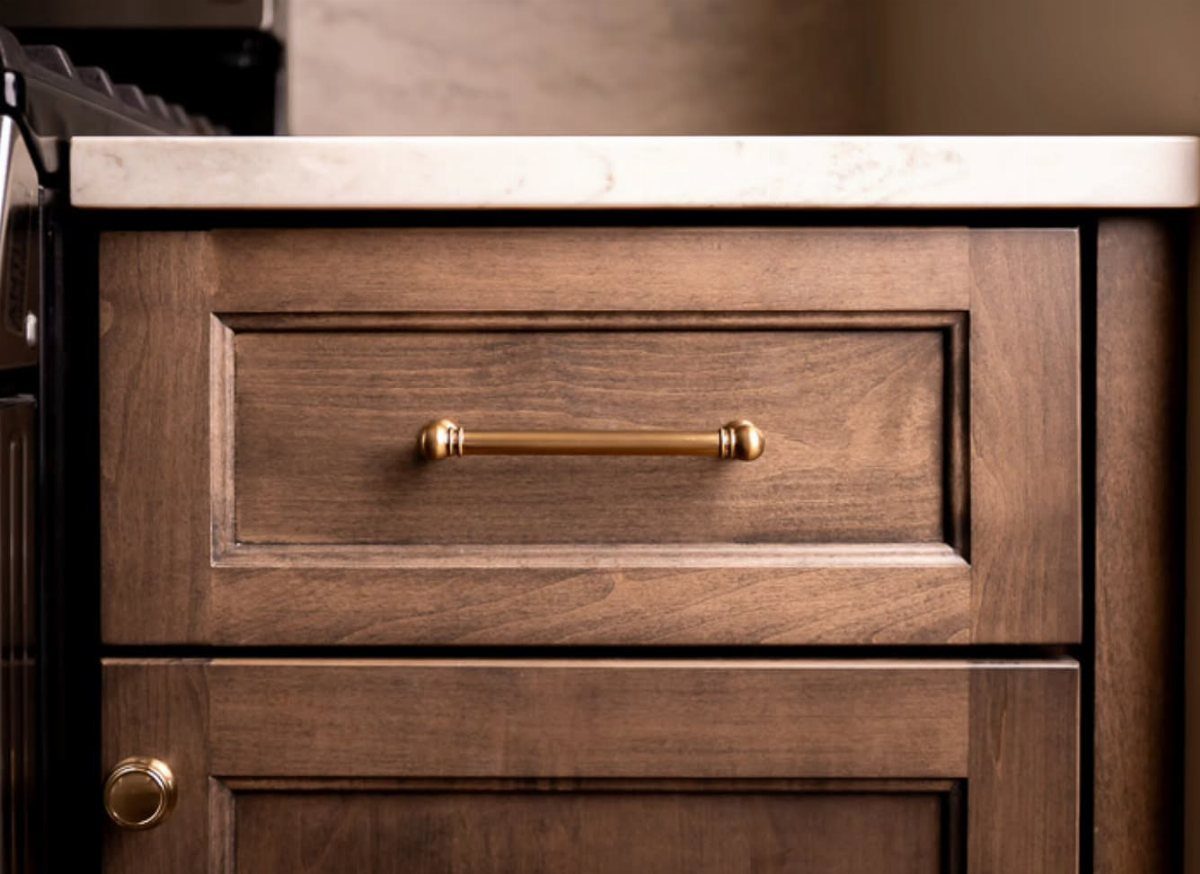 Brown stained wood kitchen drawers with matte finish and gold metal handles.