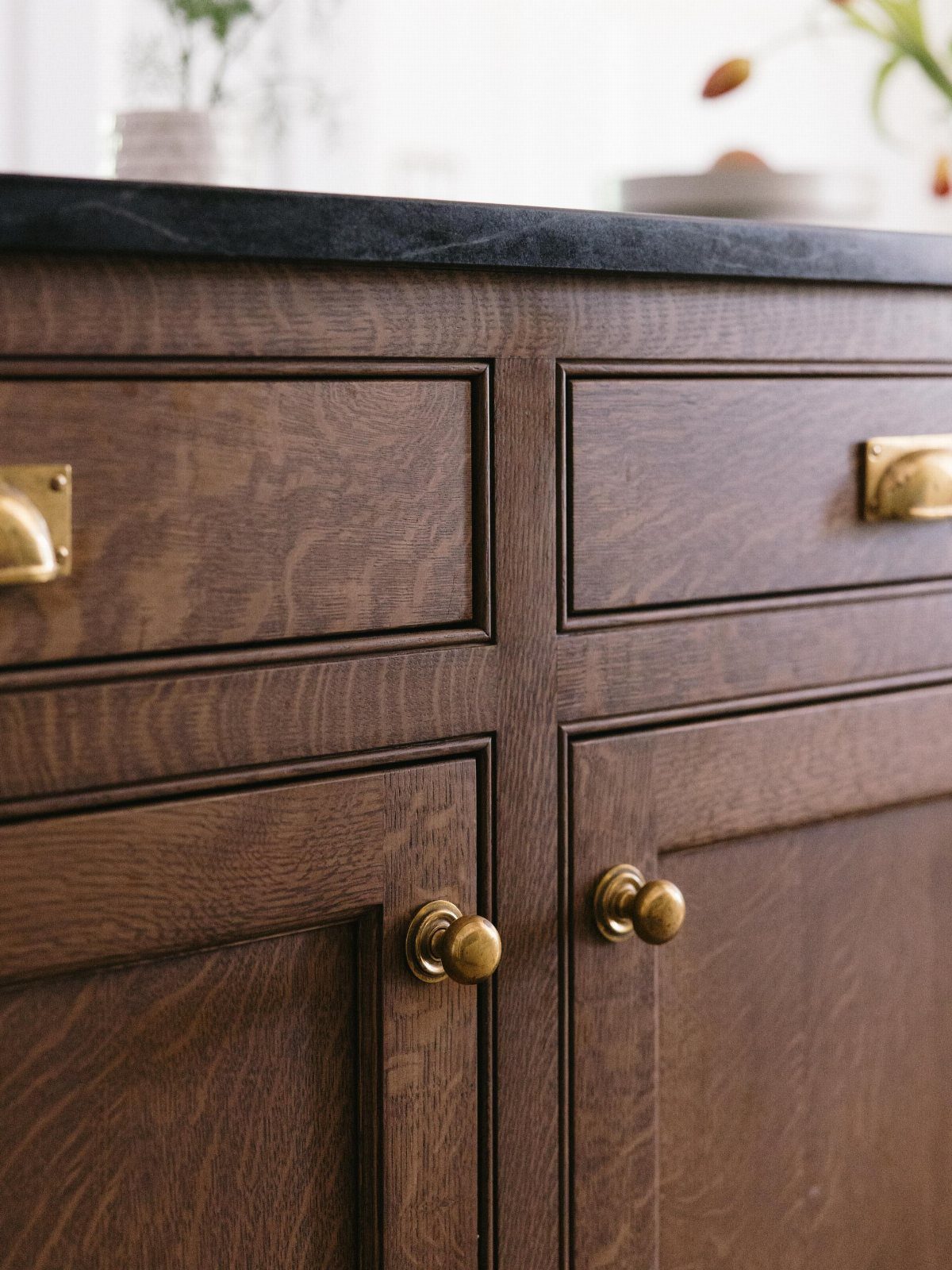 Dark brown stained wood kitchen cabinets with gold hardware and black countertop.