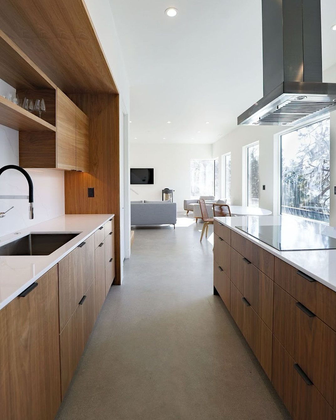 Flat panel walnut kitchen cabinets with white countertops and grey concrete flooring.