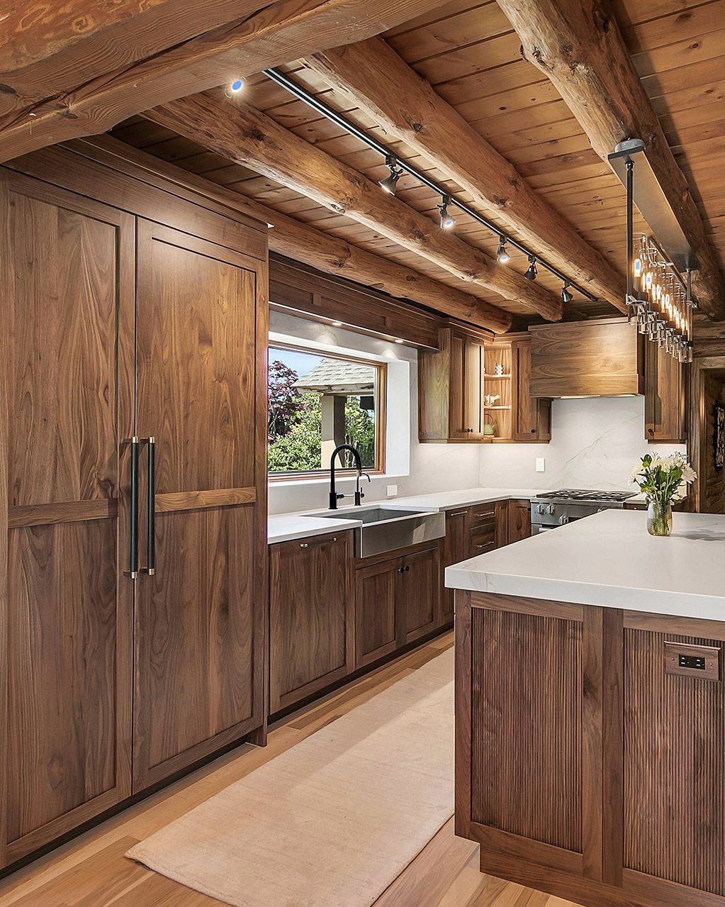 Walnut kitchen cabinets and white countertops under a rustic log beam ceiling.