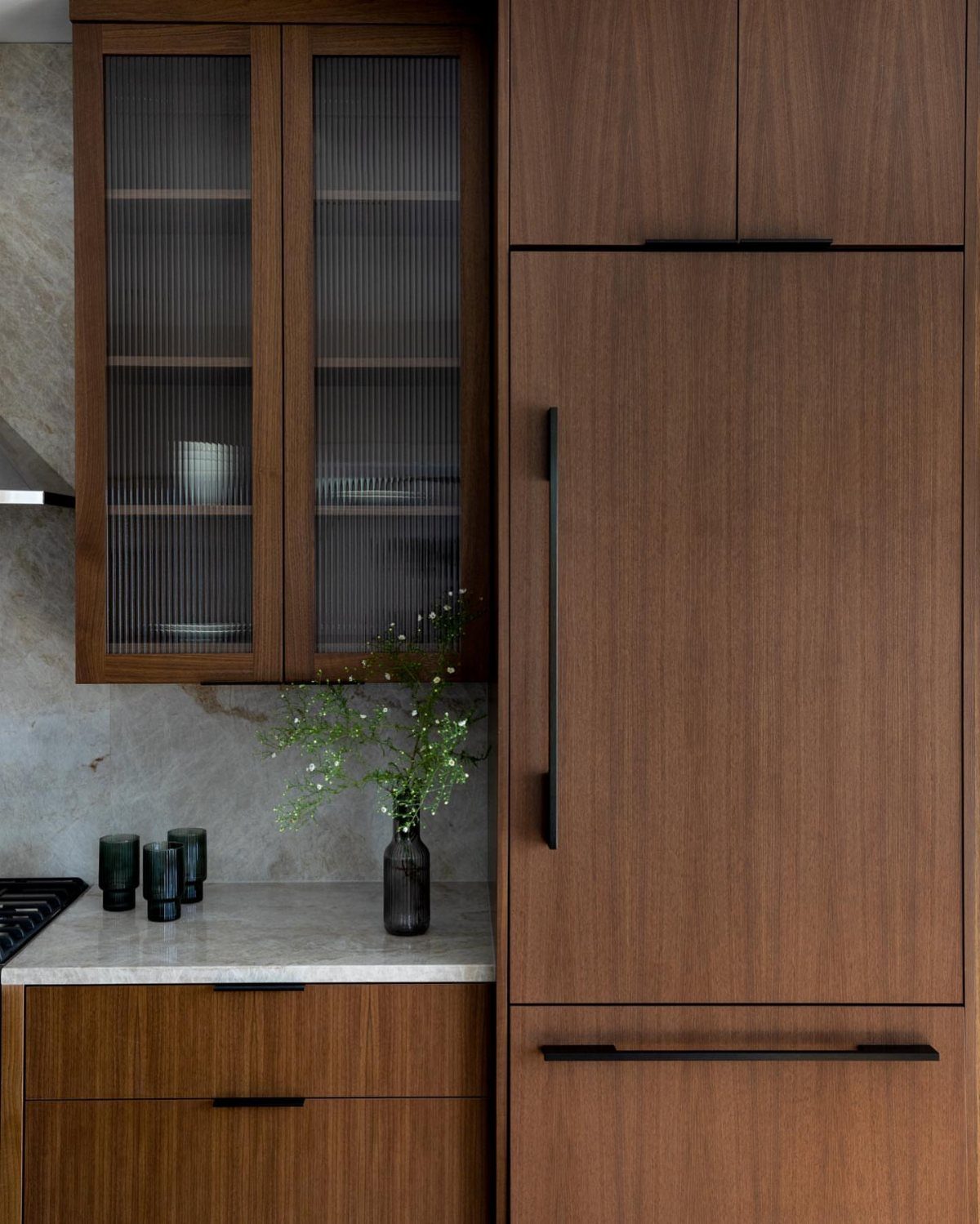 Walnut kitchen cabinets with fluted glass fronts and a white marble countertop.