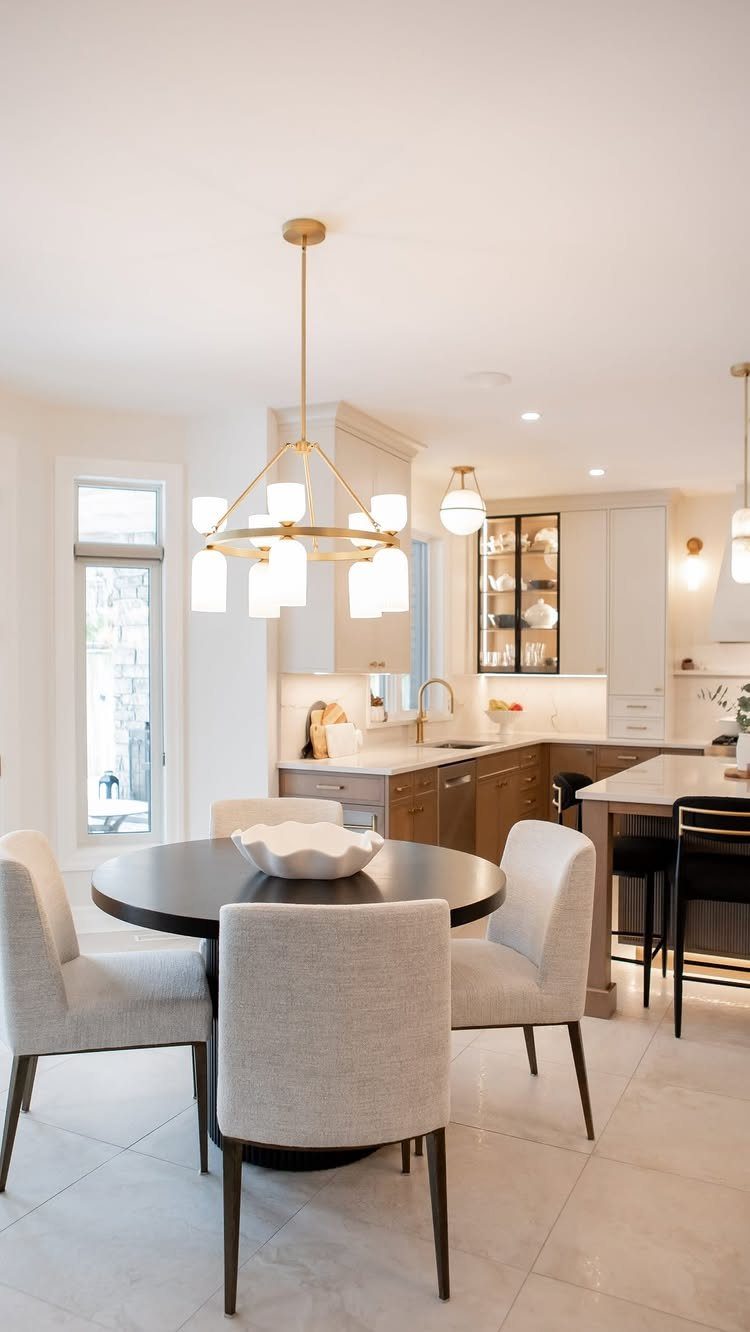 Gold circular chandelier with white shades hanging over a round dark wood dining table