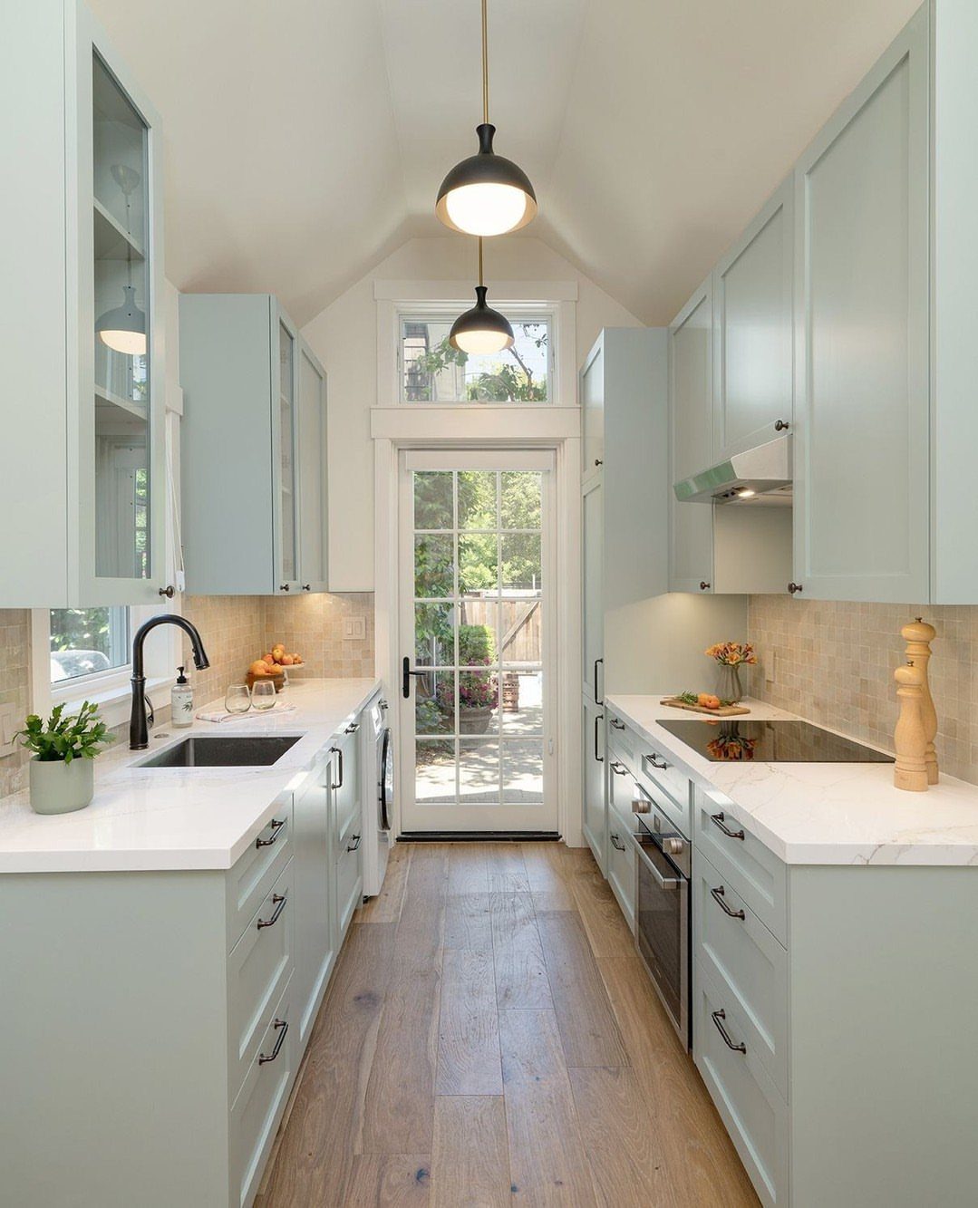 Galley kitchen with light blue cabinets and black dome pendant ceiling lights.
