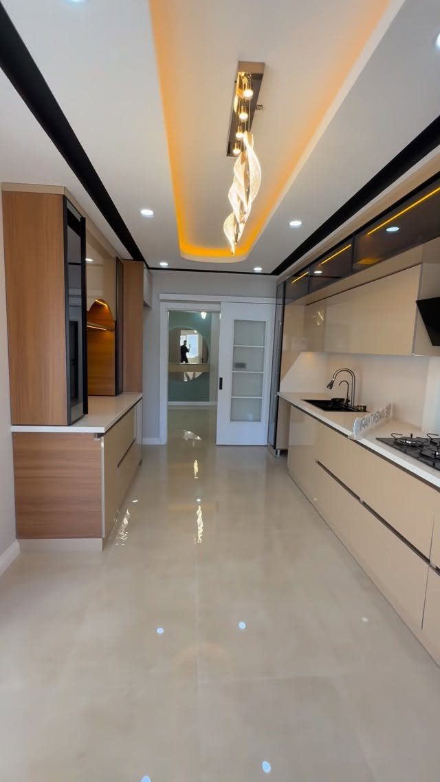 Modern galley kitchen featuring recessed orange cove lighting and a crystal pendant light.