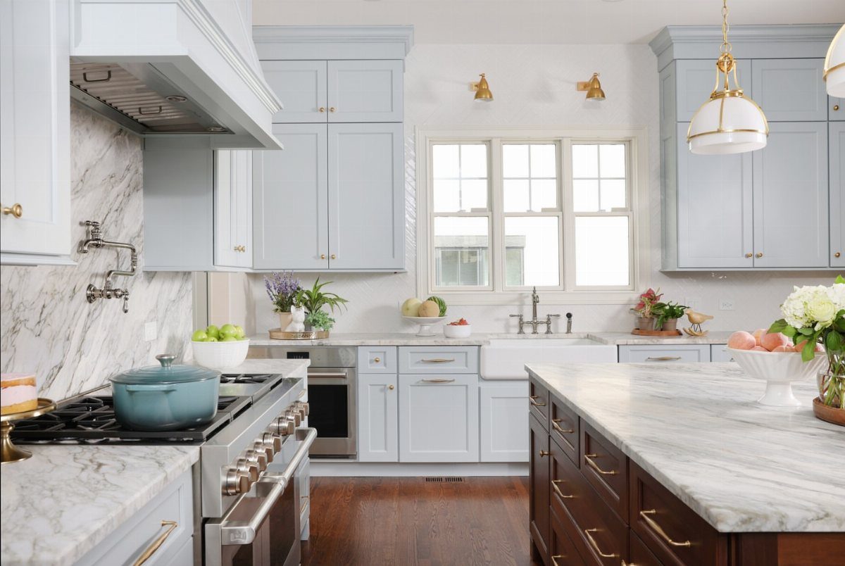 Two gold wall-mounted sconces above a kitchen window with light blue cabinets.