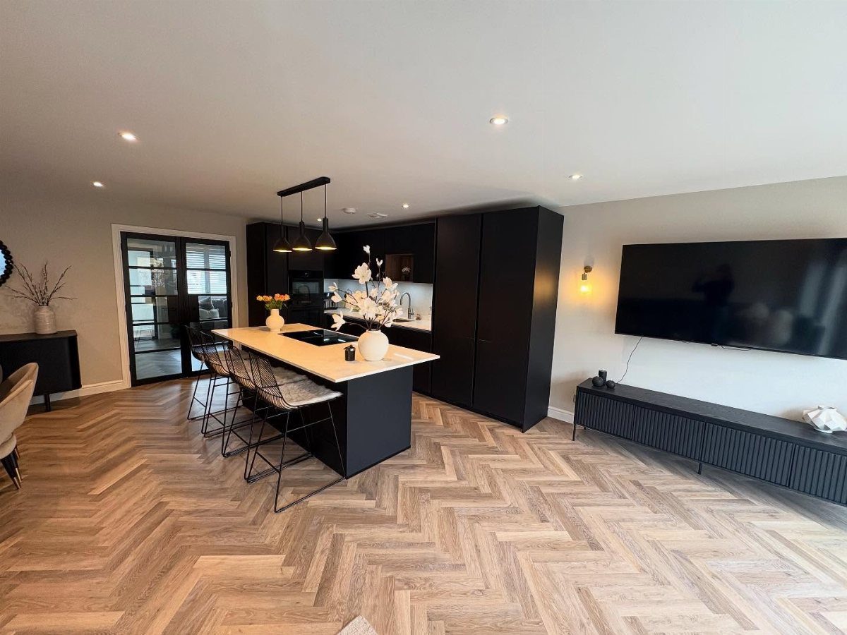 Modern open-concept living room and kitchen with black cabinetry and herringbone wood floors
