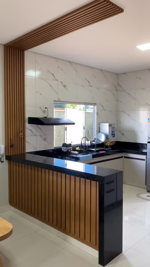 Modern kitchen with white marble tiles, black countertops, and wooden slatted breakfast bar.